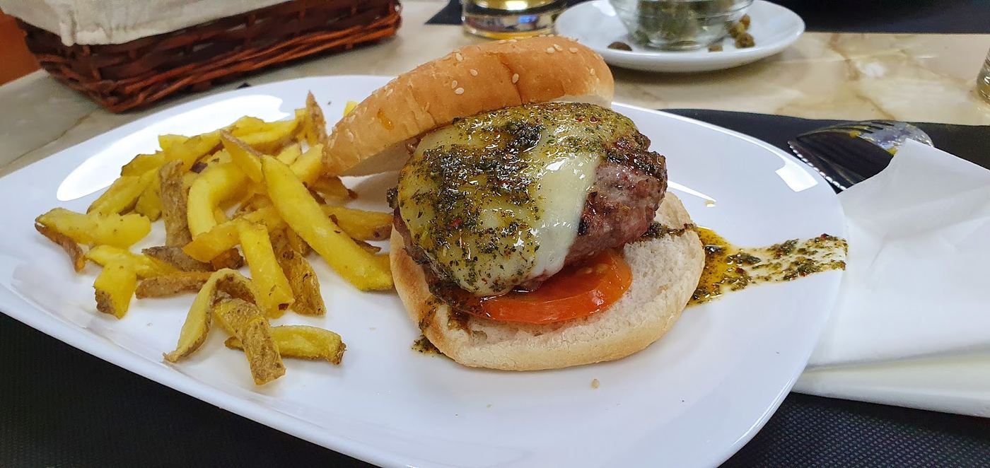 Hamburguesa gourmet con salsa chimichurri y patatas fritas.